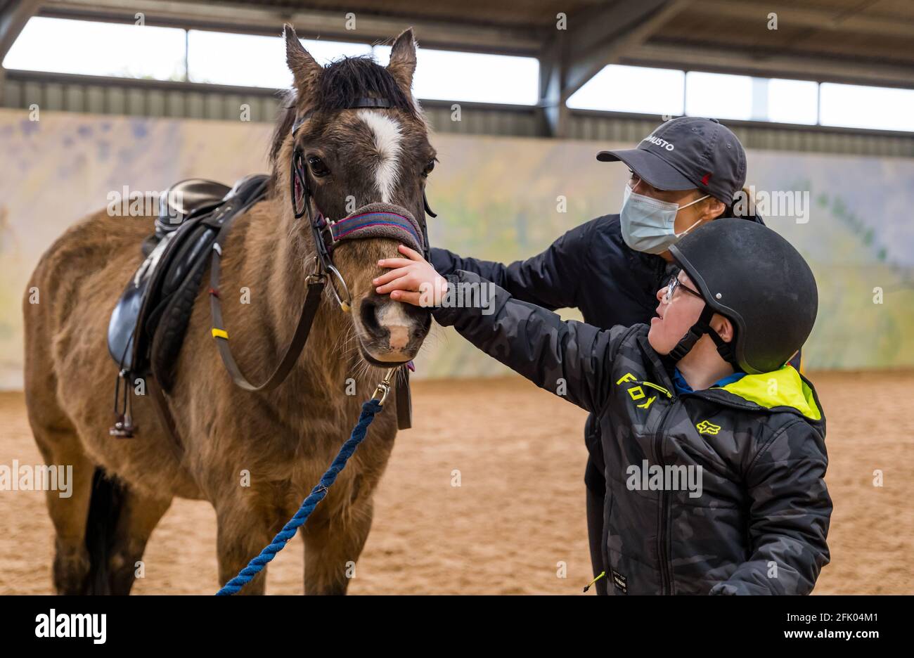 East Lothian, Écosse, Royaume-Uni, 27 avril 2021. Muirfield Riding Therapy rouvre: L'organisme de bienfaisance accueille ses premiers jeunes pour leur séance de thérapie avec des restrictions de verrouillage assouplies. En raison de restrictions continues, seuls les clients plus mobiles peuvent être pris en charge pour le moment. Photo: Fin, 10 ans, un élève de l'école primaire de yester donne à son cheval de thérapie Briony un pat avec sa mère Banque D'Images