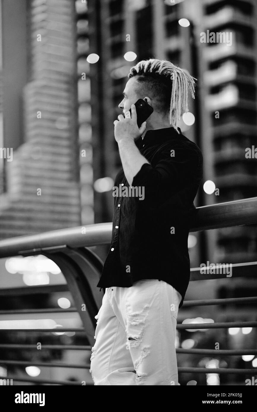 Portrait en noir et blanc d'un homme d'affaires moderne avec une coiffure moderne parle par smartphone sur fond de mégapole Banque D'Images