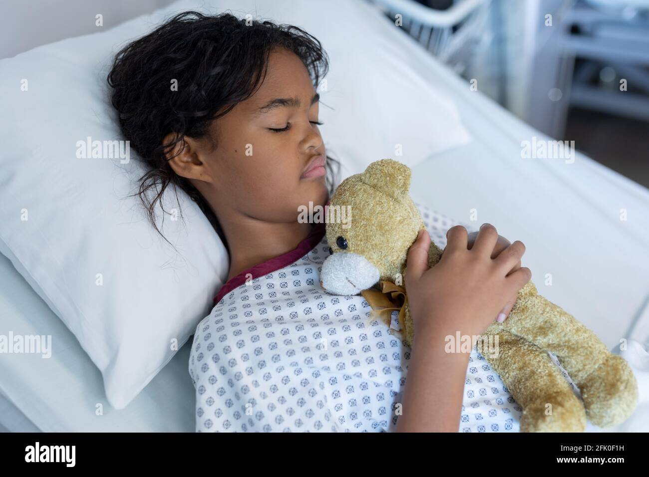 Race mixte fille malade tenant l'ours en peluche couché dedans lit dans une salle d'hôpital Banque D'Images