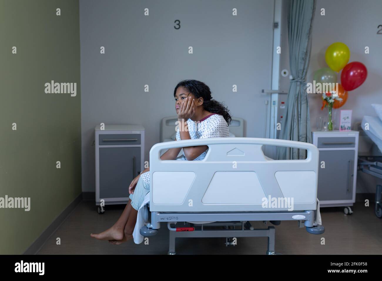 S'ennuyer malade de race mixte fille assis sur le lit d'hôpital reposant tête à portée de main Banque D'Images