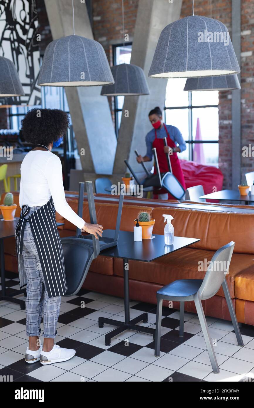 Divers serveurs masculins et féminins portant des masques faciaux nettoyer les tables dans le café Banque D'Images