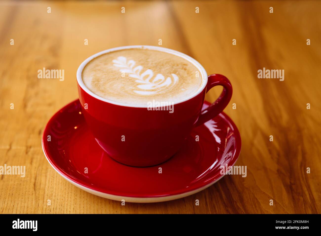 Café aromatique dans une tasse rouge avec mousse de lait et latte art sur une table en bois clair. Banque D'Images