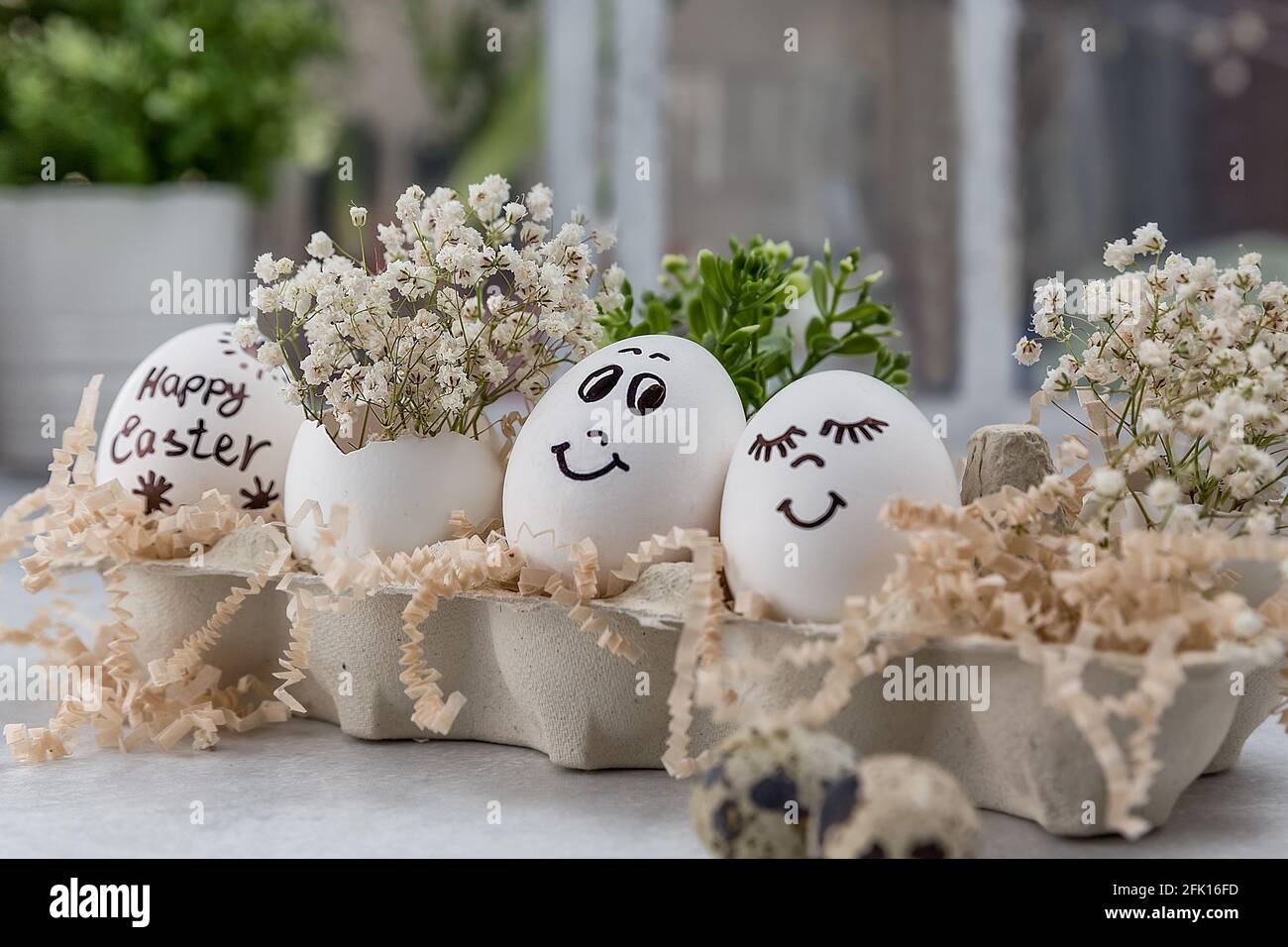 Composition de Pâques. Œufs blancs aux visages amusants peints sur la table. Un petit bouquet dans un œuf. Le concept minimal de Pâques. Une carte de Pâques avec un Banque D'Images