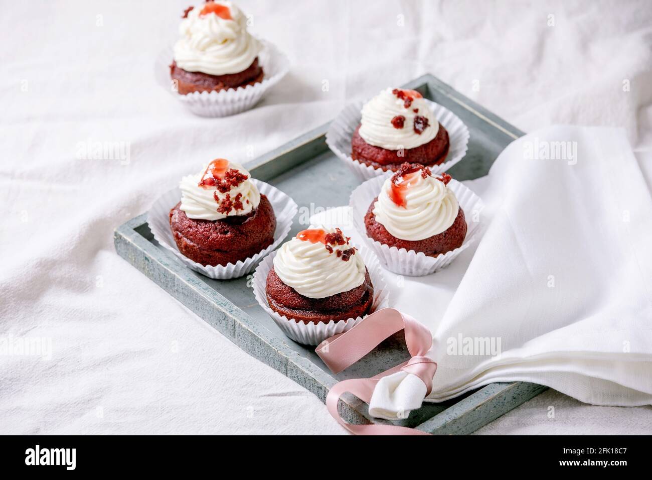 Petits gâteaux faits maison en velours rouge avec crème fouettée sur plateau en bois, serviette blanche avec ruban sur nappe blanche. Banque D'Images
