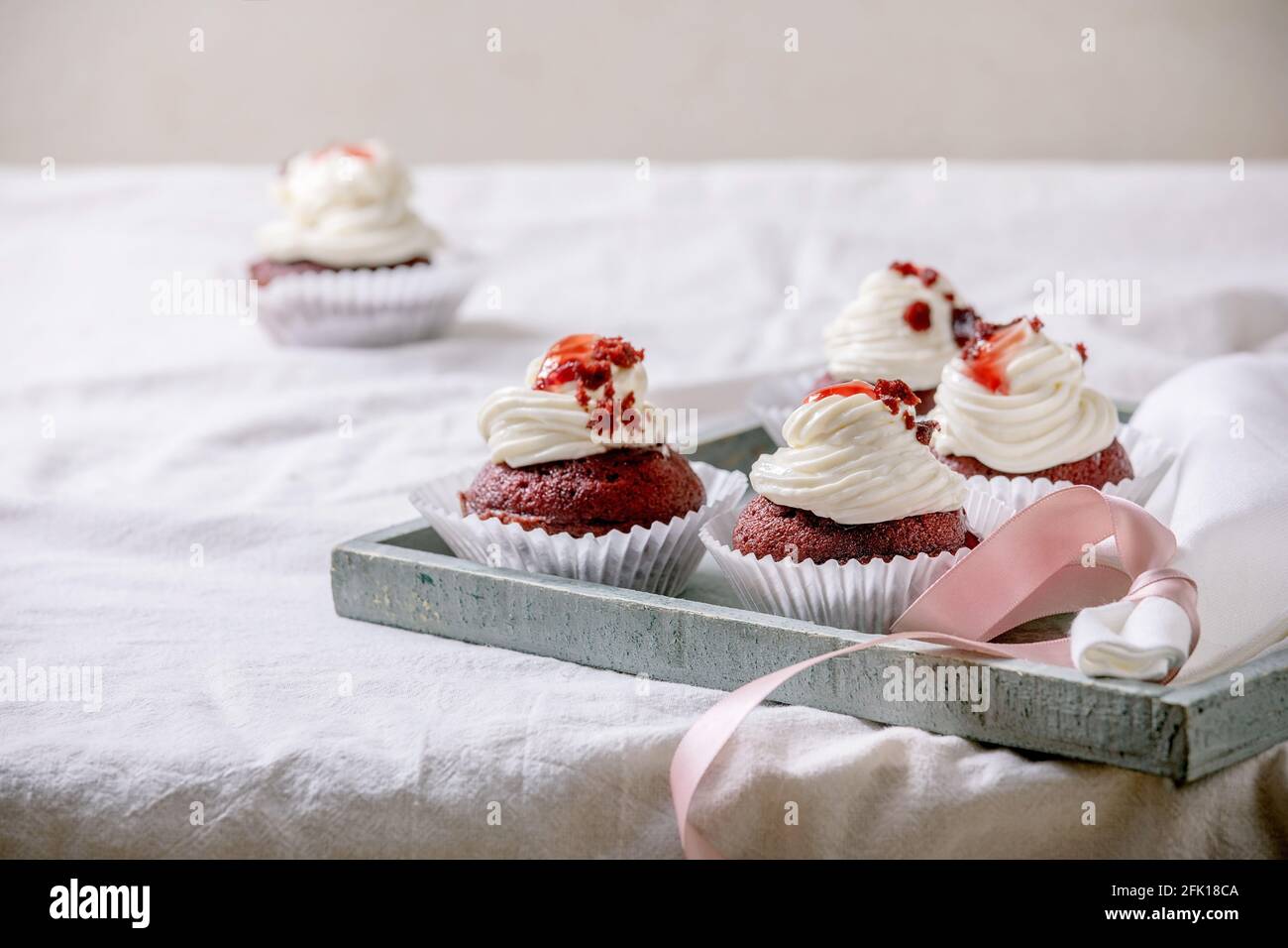Petits gâteaux faits maison en velours rouge avec crème fouettée sur plateau en bois, serviette blanche avec ruban sur nappe blanche. Banque D'Images