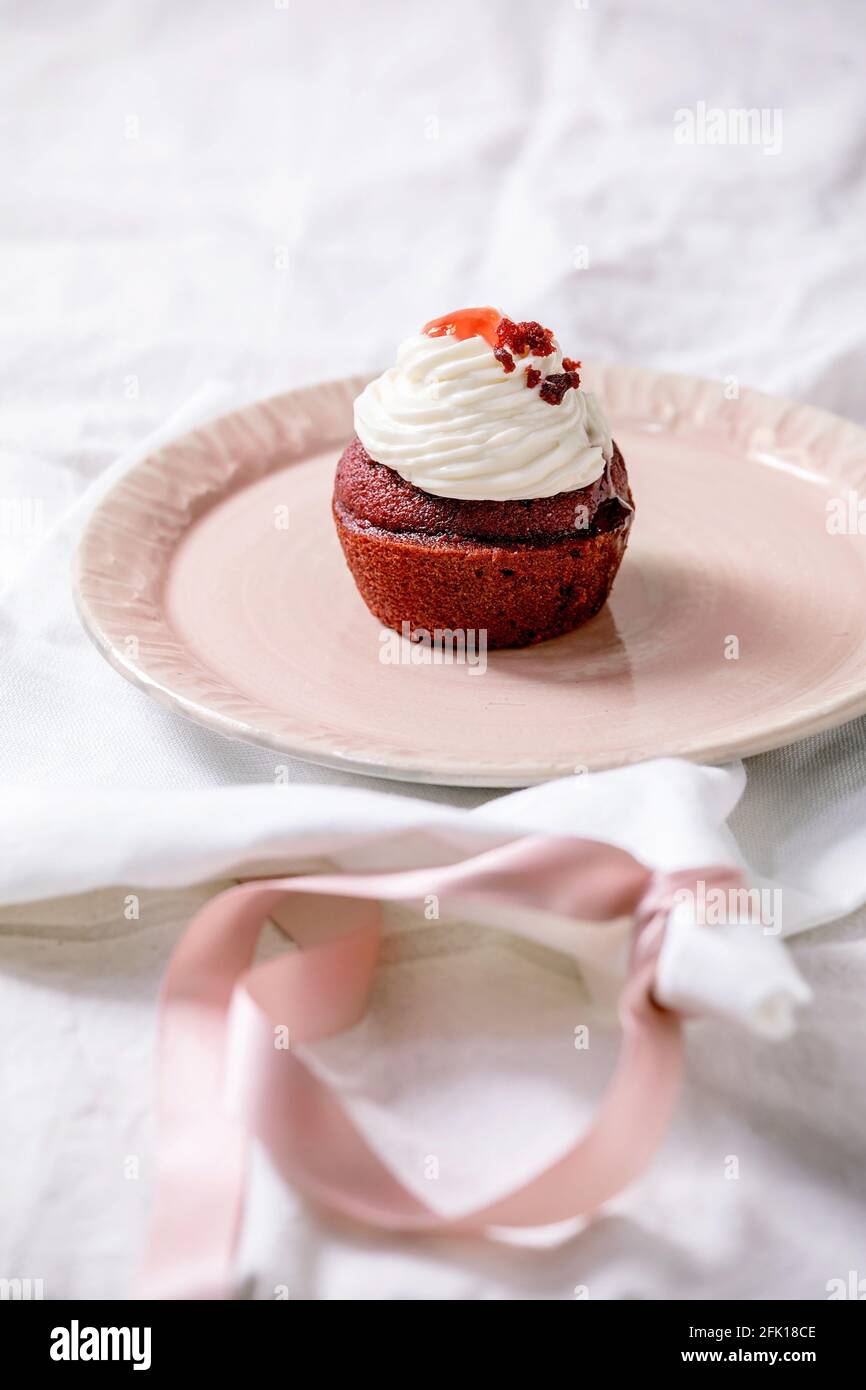 Petit gâteau en velours rouge maison avec crème fouettée sur plaque en céramique rose, serviette blanche avec ruban sur nappe blanche. Copier l'espace Banque D'Images