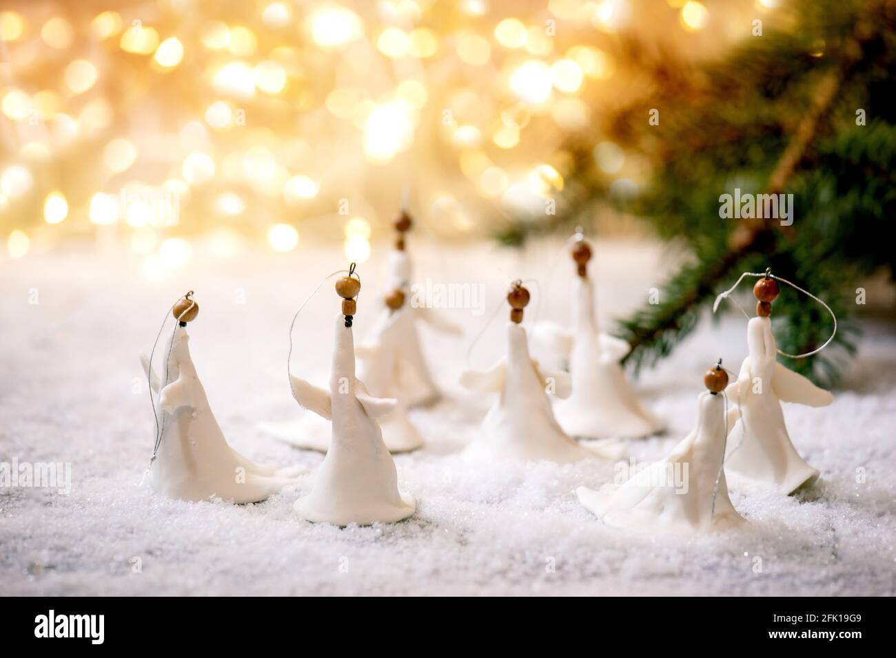 Anges de Noël en porcelaine. Ensemble de décorations artisanales de Noël faites à la main sur la neige avec des lumières de Noël bokeh et des branches de sapin. Banque D'Images