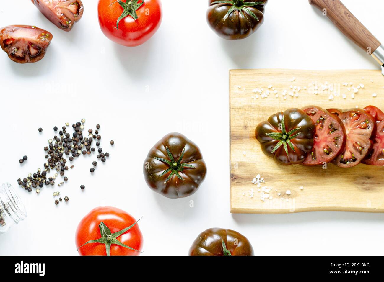 Couper et des tomates rouges entières sur une planche à découper en bois et arrière-plan blanc Banque D'Images