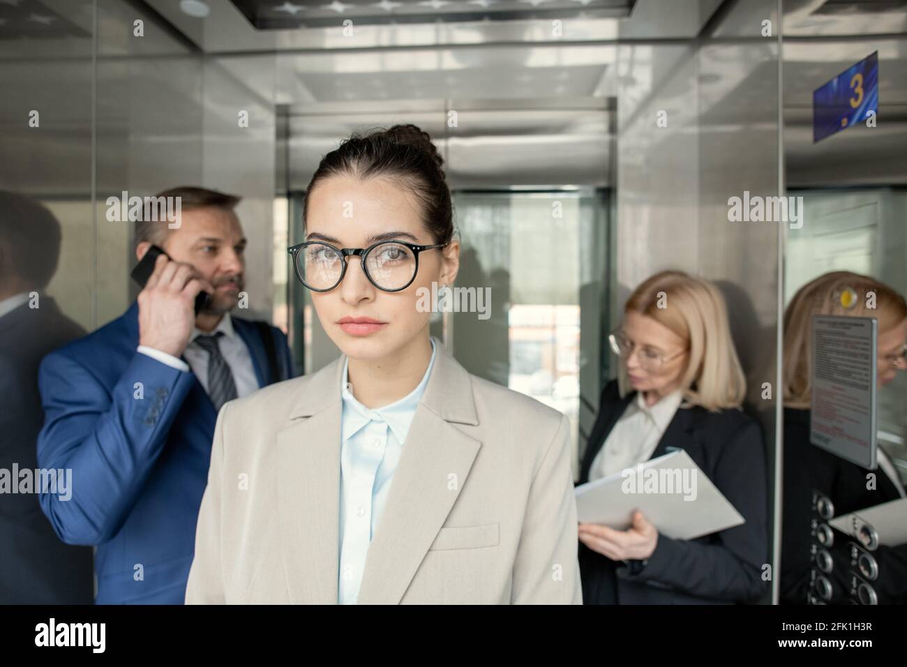 Portrait d'une femme d'affaires sérieuse attrayante debout dans un ascenseur avec personnes occupées en arrière-plan Banque D'Images