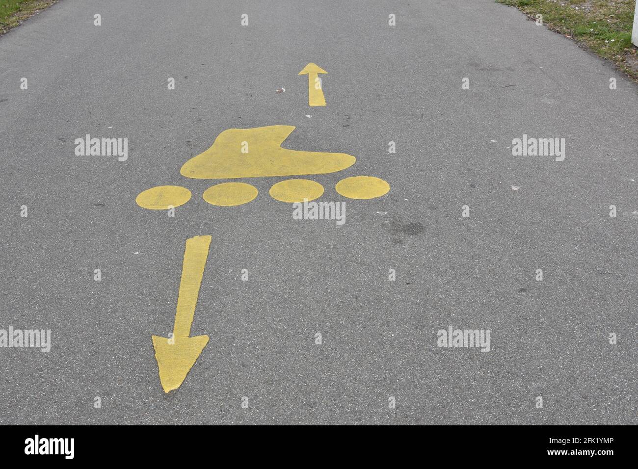 Les lames à rouleaux sont en train d'asphalter des chenilles avec des icônes jaunes de patins à roulettes et des flèches dans des directions opposées. Piste de patinage pour le sport et les loisirs. Banque D'Images