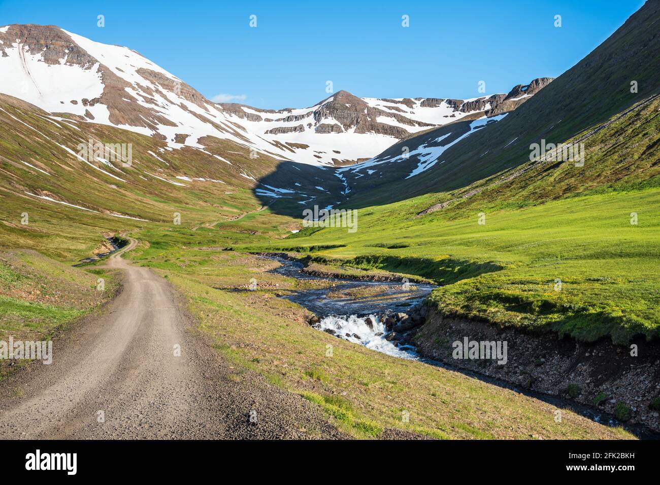 Route sinueuse déserte le long d'une crique à pied de sommets enneigés dans un paysage de montagne majestueux sur un jour d'été ensoleillé Banque D'Images