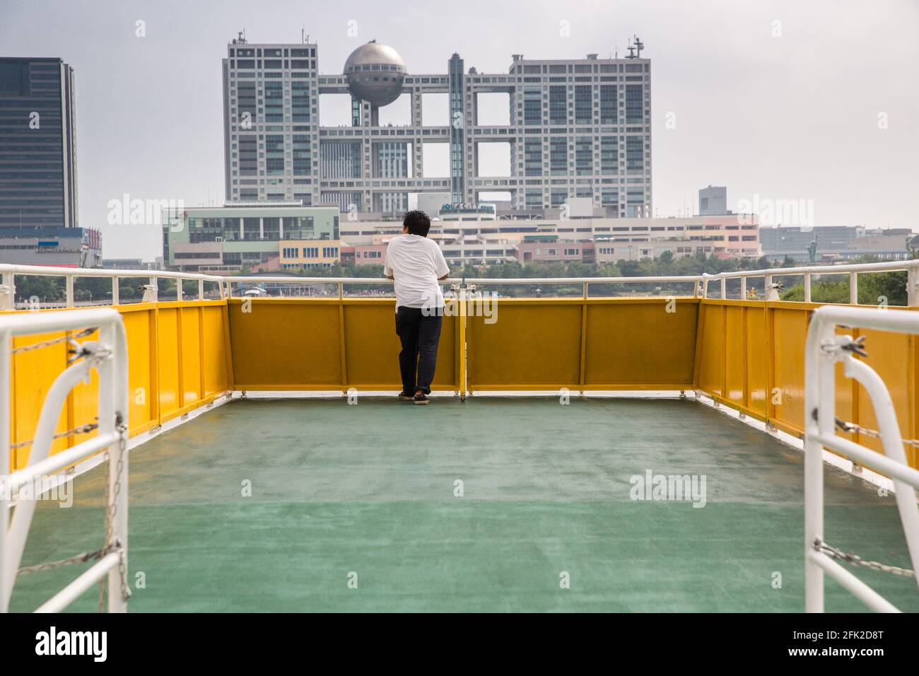 Seul homme japonais sur le bateau. Odaiba ferry avec l'île d'Odaiba et Aqua City au loin. Tokyo, Japon Banque D'Images