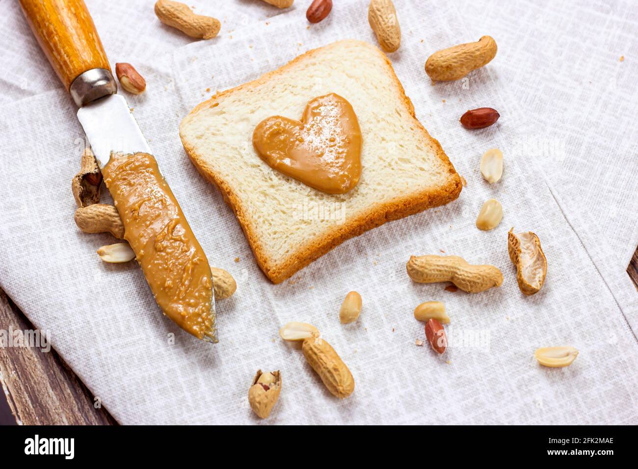 Toasts faits maison pour le petit-déjeuner avec beurre d'arachide en forme de cœur frais et noix sur fond textile léger. Banque D'Images