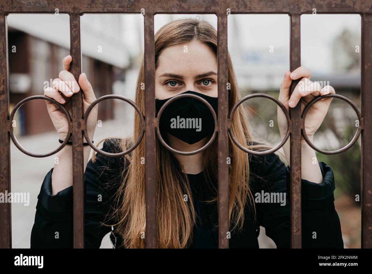 femme avec masque de visage derrière les barres à l'extérieur, concept lockdown covid 19 Banque D'Images