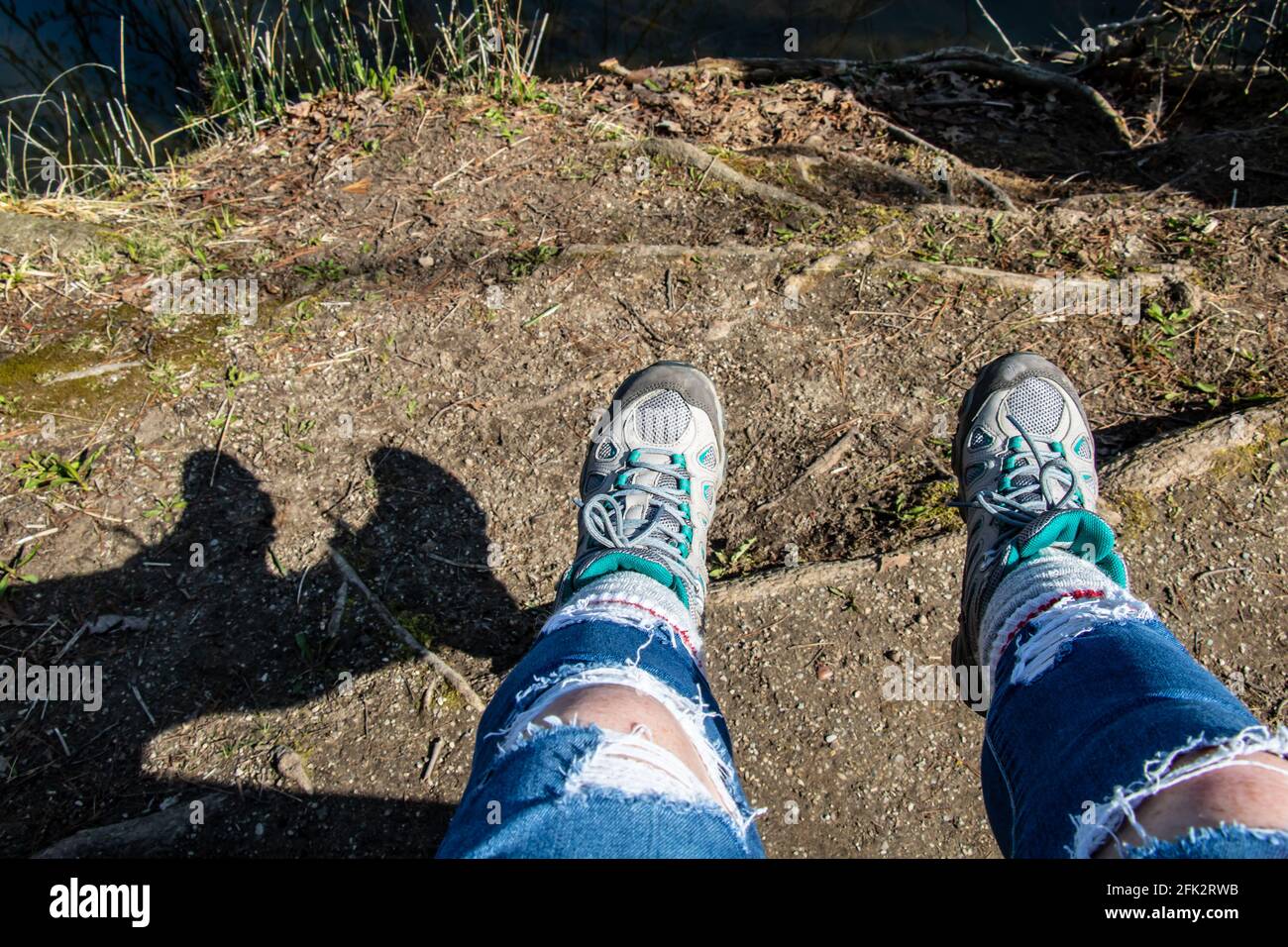 Les jambes de la femme pendaient d'un banc, les pieds balancé vers l'avant au-dessus de terre. L'ombre de ses jambes est visible, avec des jeans déchirés et des bottes de randonnée. Banque D'Images