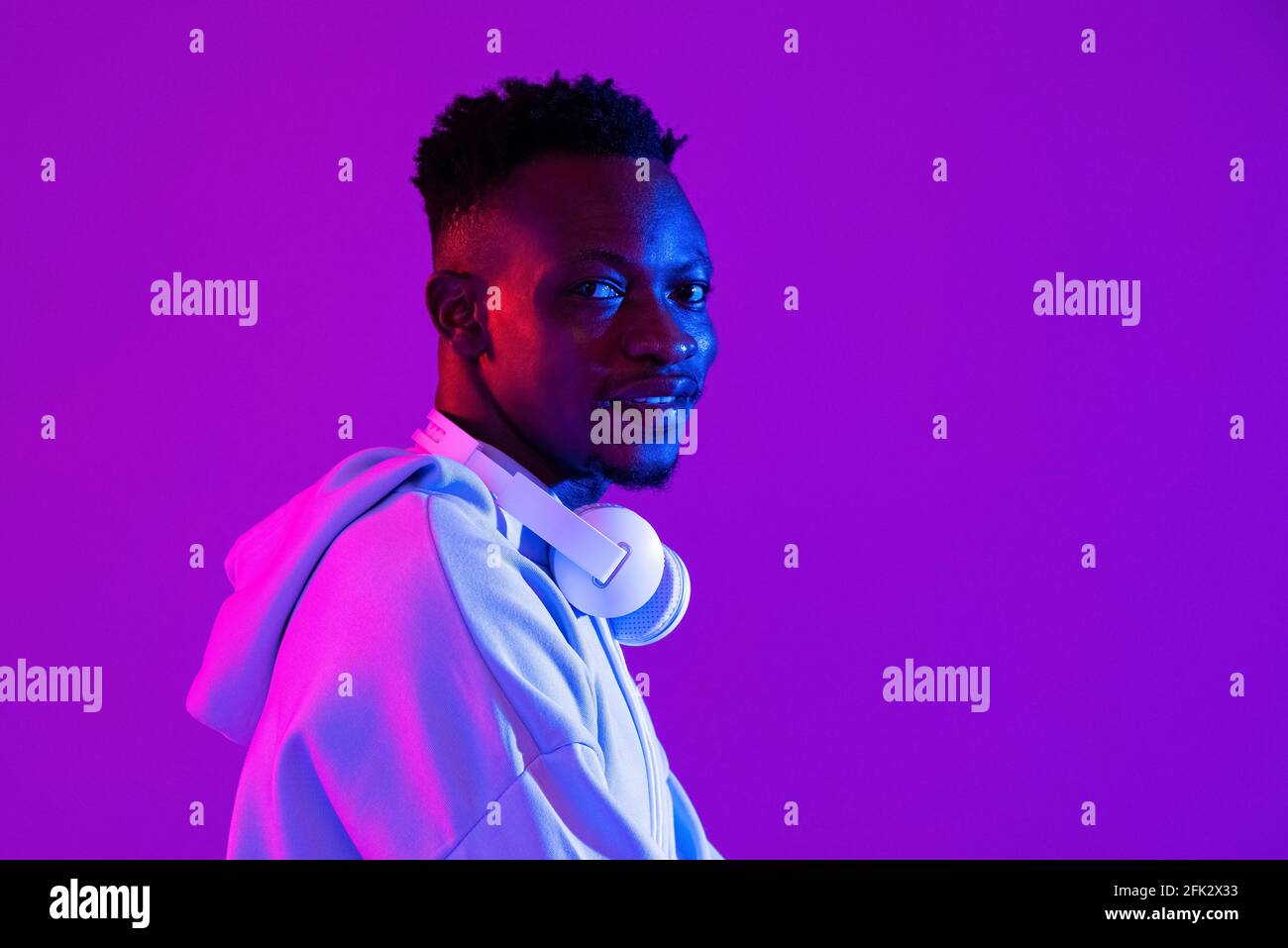 Jeune homme africain élégant avec écouteurs au néon futuriste violet arrière-plan studio léger Banque D'Images