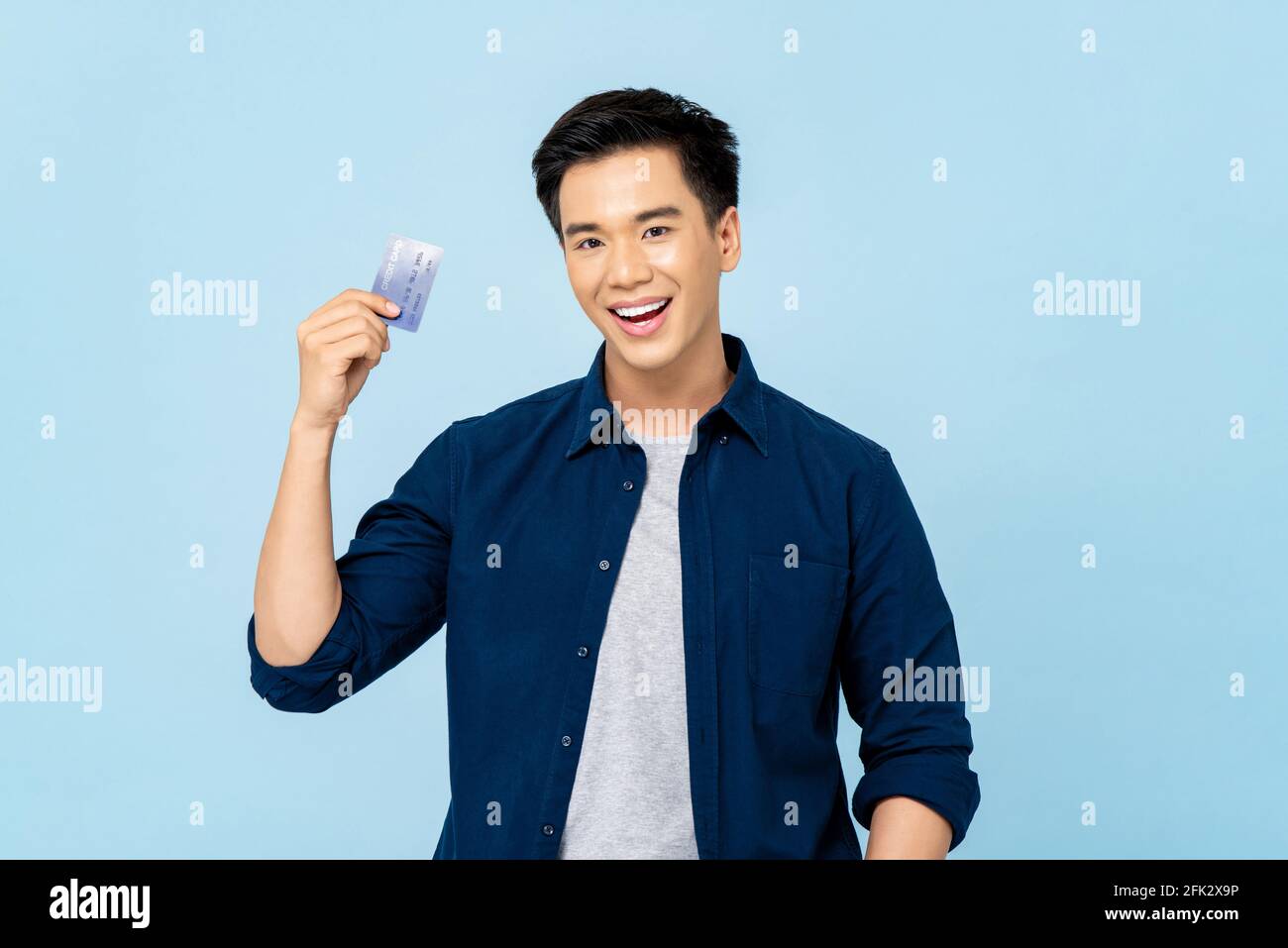 Portrait d'un jeune homme asiatique beau et souriant tenir la carte de crédit dans un arrière-plan bleu clair isolé Banque D'Images