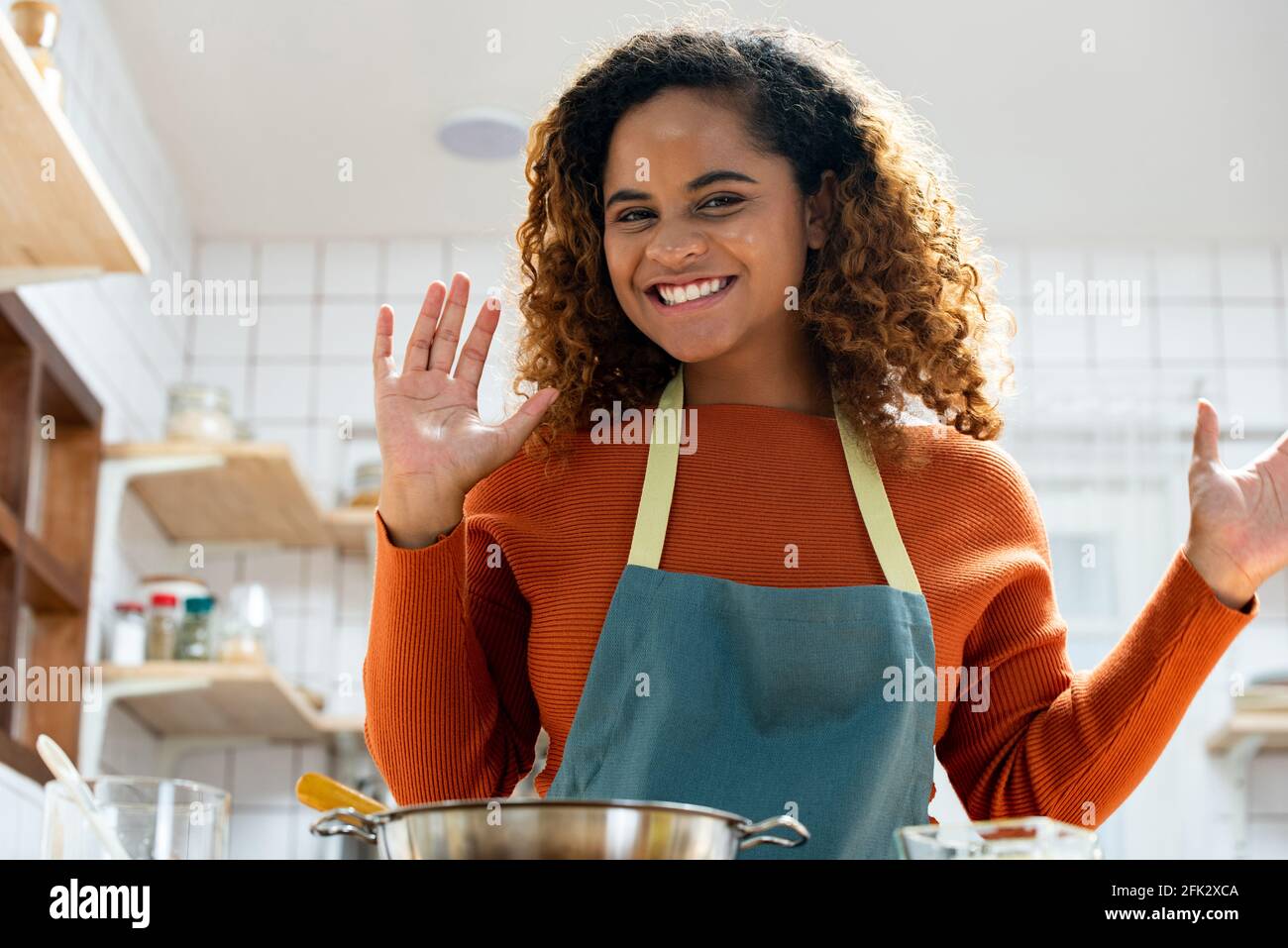 Jeune femme afro-américaine heureuse qui se fait passer les mains à la caméra passer un appel vidéo dans la cuisine à la maison Banque D'Images