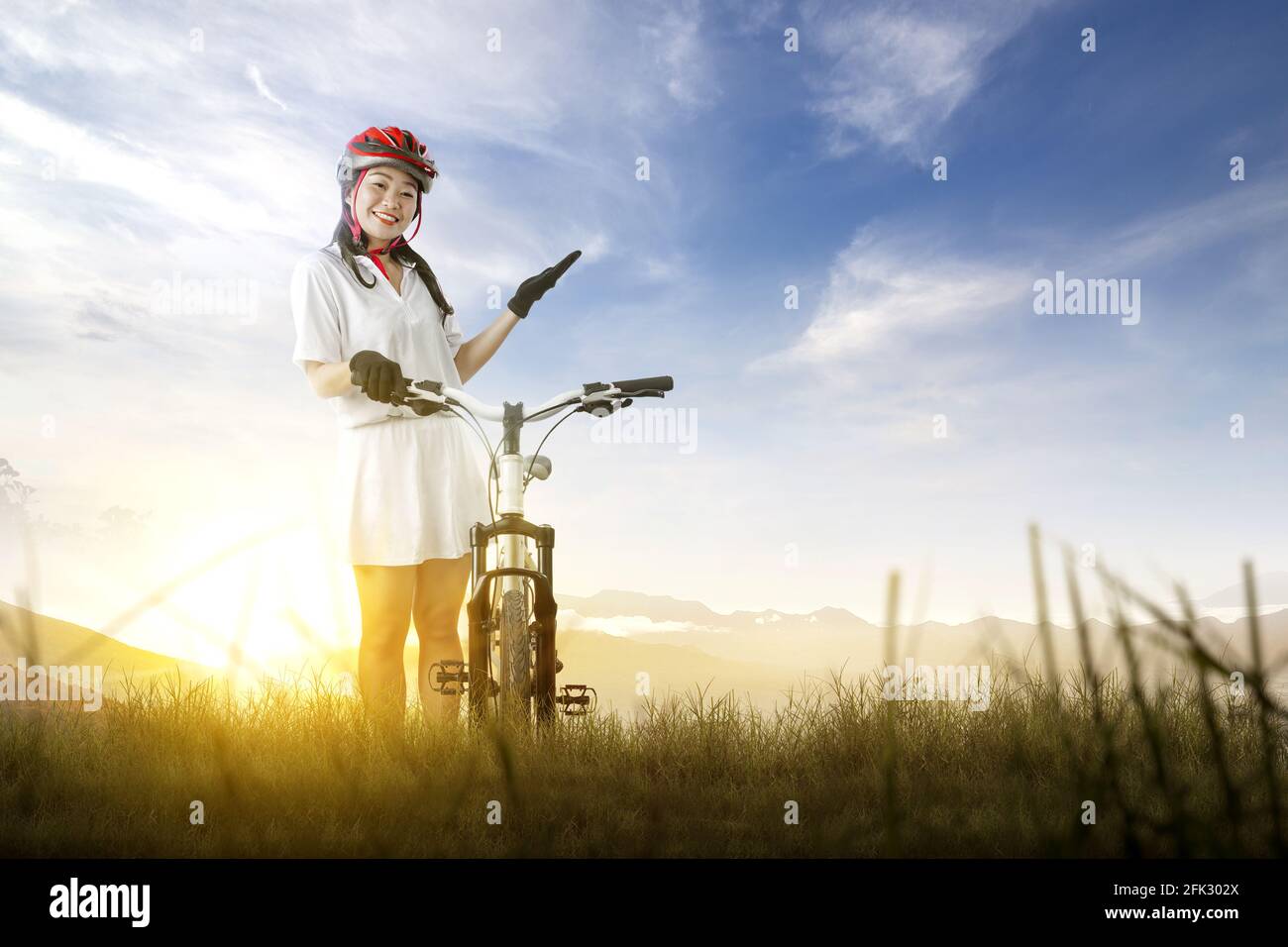 Femme asiatique avec un casque de vélo debout à côté de son vélo sur le champ de prairie. Journée mondiale du vélo Banque D'Images