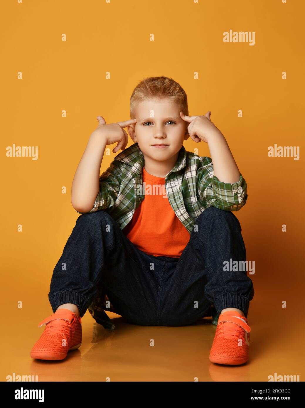 L'adolescent élégant est un t-shirt à carreaux, un t-shirt orange et un Jean  qui tient les doigts à la tête et fait des gestes Photo Stock - Alamy
