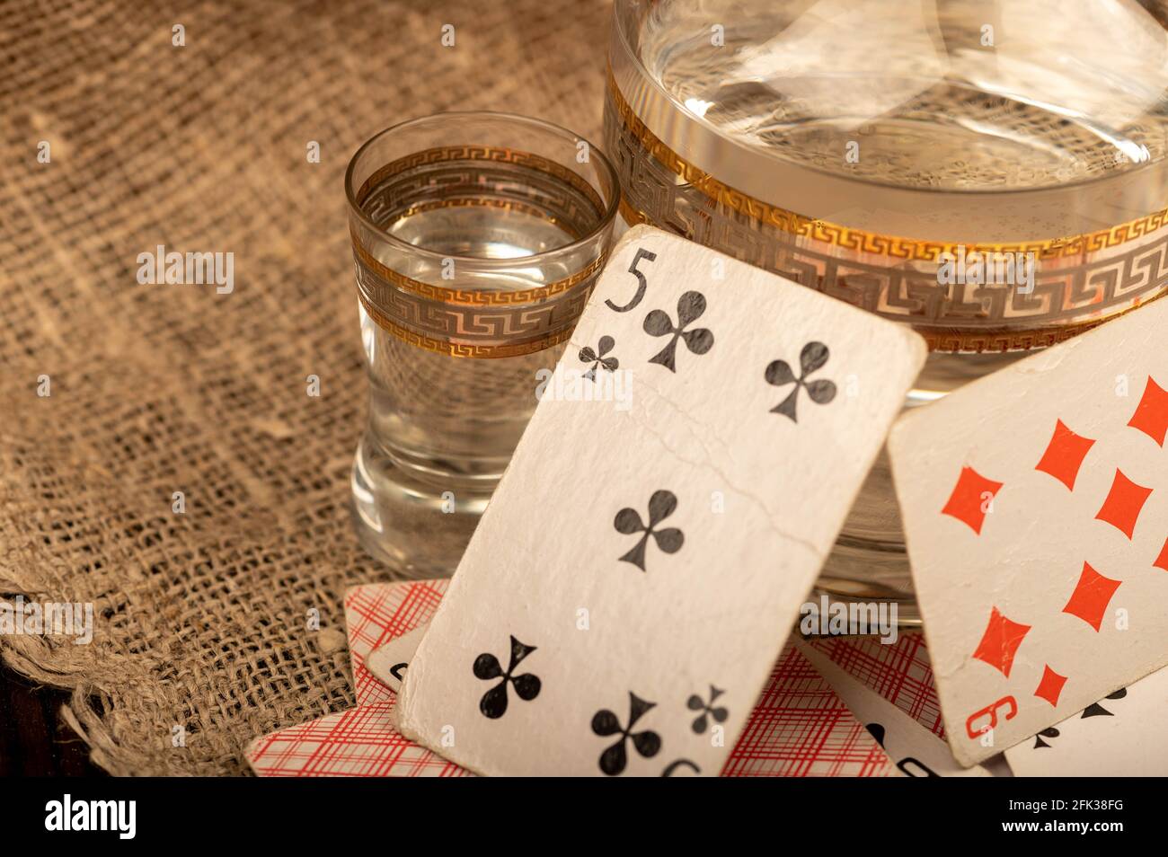 Jouer aux cartes, un verre de vodka et un carafe de vodka sur une table recouverte de gros burlap. Gros plan, mise au point sélective. Banque D'Images