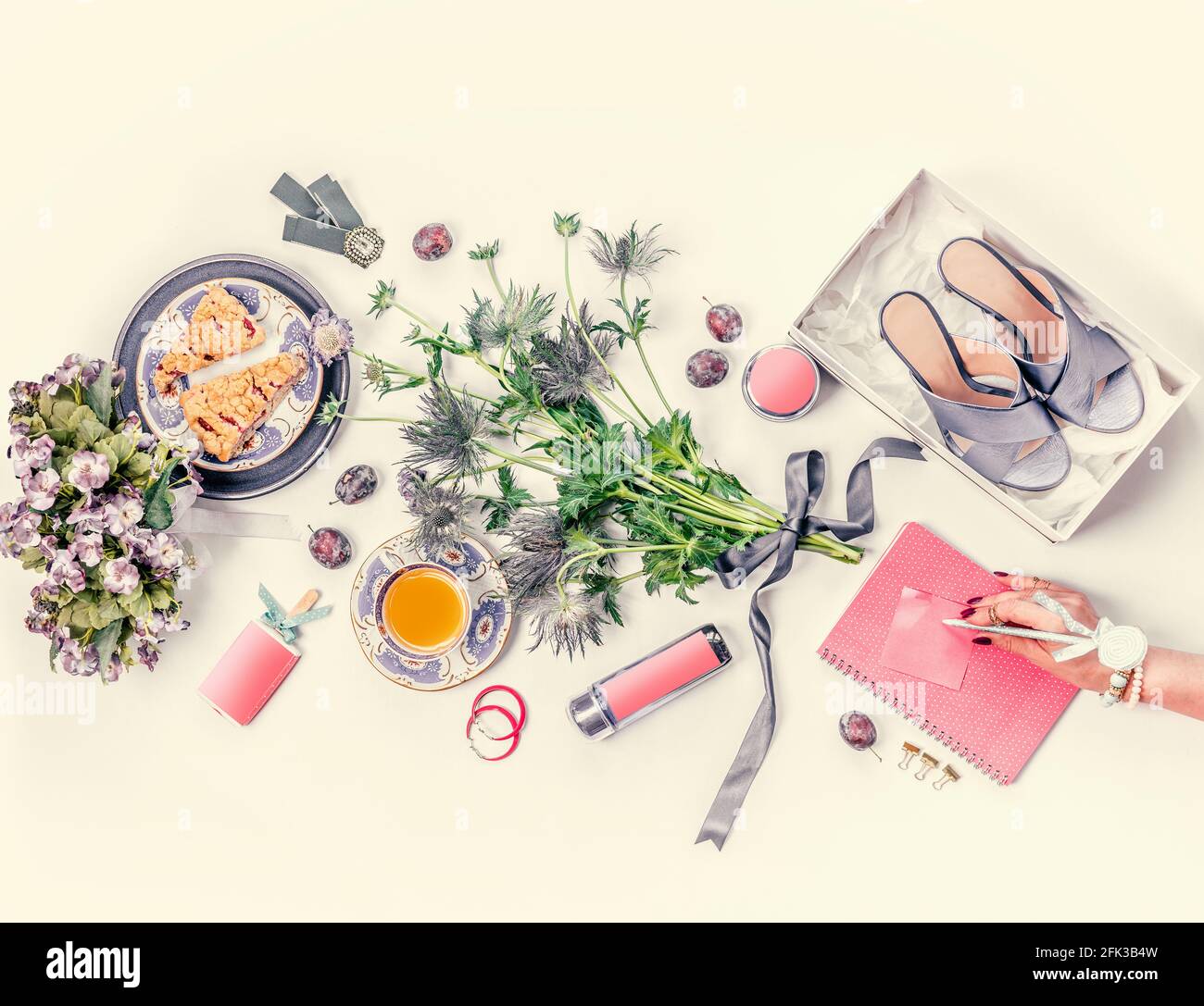 Femme main avec rose carnet style de vie plat avec bleu nouveau talons hauts chaussures dans boîte, bouquet de fleurs, tasse de thé, gâteaux, bijoux, cosmétiques, fr Banque D'Images