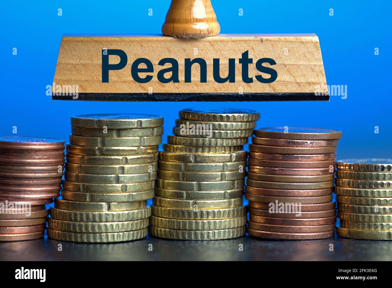 Allemagne. 27 avril 2021. Un timbre en bois avec l'inscription « Peanuts » sur plusieurs piles de pièces en euros/centimes. Photo avec composition sur fond bleu. Les arachides sont familièrement une expression pour de petites choses ou des sommes insignifiantes d'argent. Le mot a été déclaré le mot allemand de l'année 1994 | usage dans le monde crédit: dpa/Alay Live News Banque D'Images
