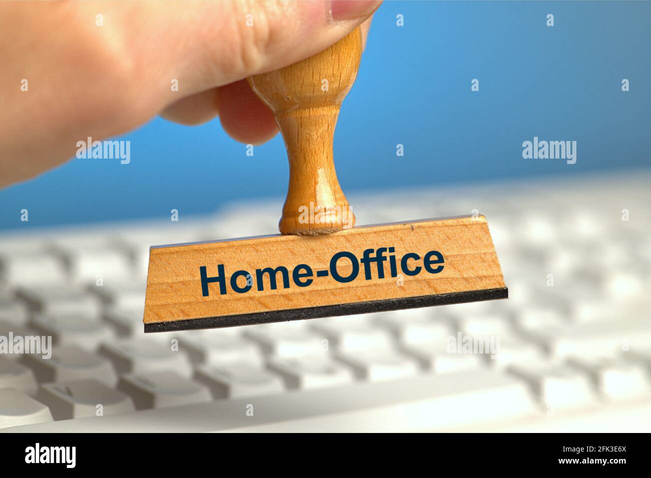 Allemagne. 22 avril 2021. Un timbre en bois avec l'inscription « Home-Office », tenu à la main dans un fond perdu sur un clavier d'ordinateur blanc. Photo avec composition sur fond bleu. Le bureau à domicile est à l'ordre du jour et est recommandé par des experts dans la mesure du possible. | utilisation dans le monde crédit: dpa/Alay Live News Banque D'Images