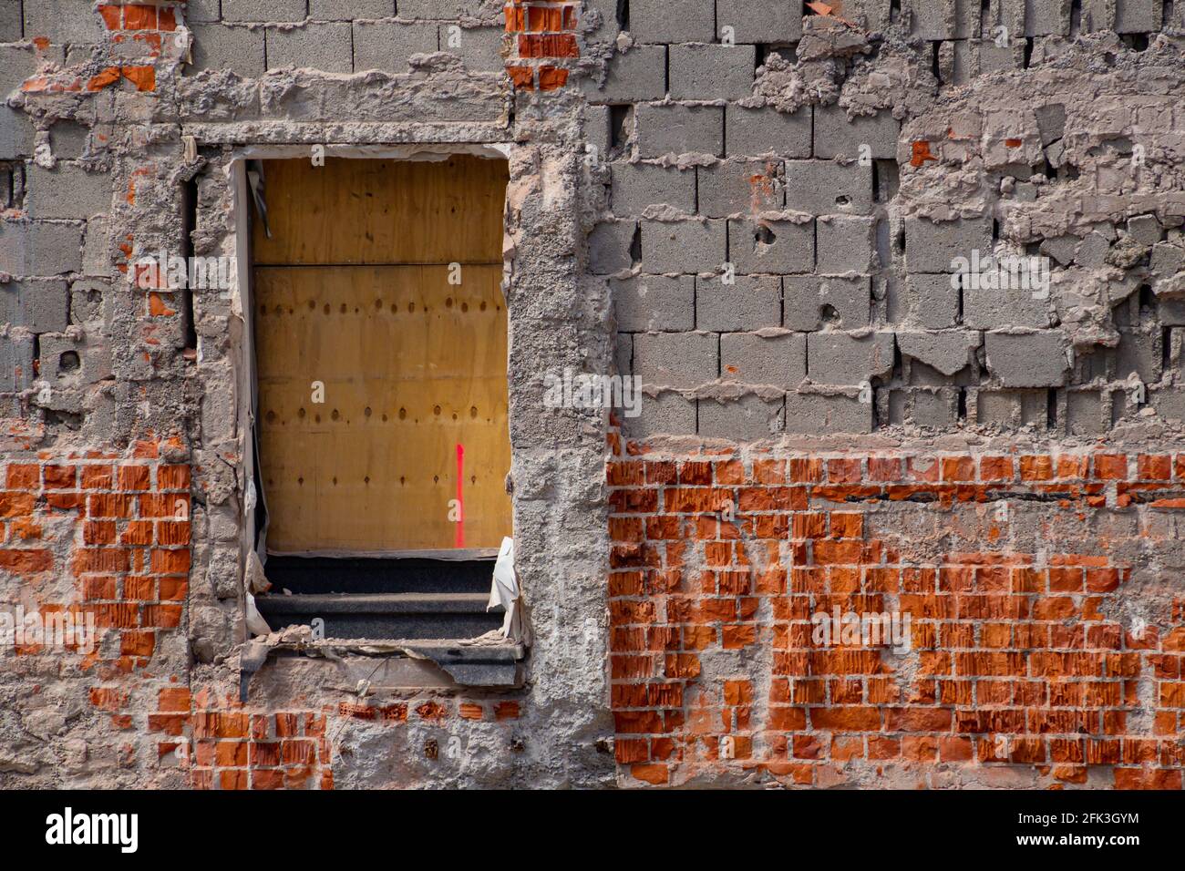 Bloc de ciment creux et mur de brique rouge d'un déchiré bâtiment en bas avec une porte couverte de lambris Banque D'Images
