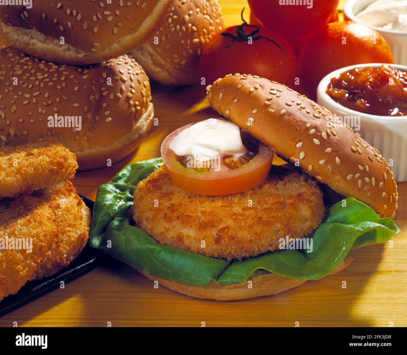 Hamburger de poulet en pain semé avec laitue, tranche de tomate et crème sure, tomates, relish, petits pains et hamburgers sur fond de bois clair Banque D'Images