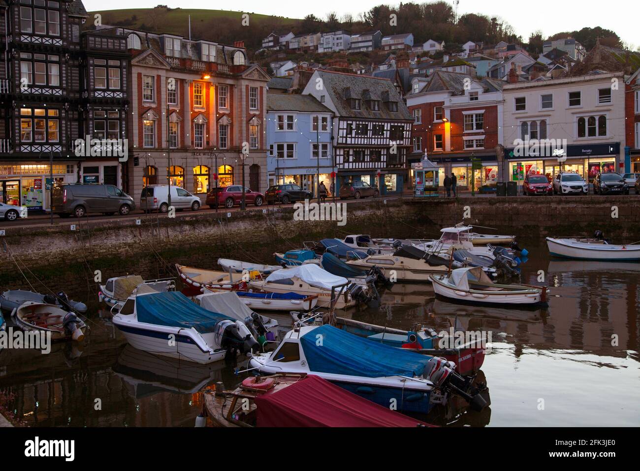 Prise de vue au crépuscule dans le port intérieur de Dartmouth avec boutiques éclairées et bateaux amarrés. Devon Angleterre, Royaume-Uni Banque D'Images