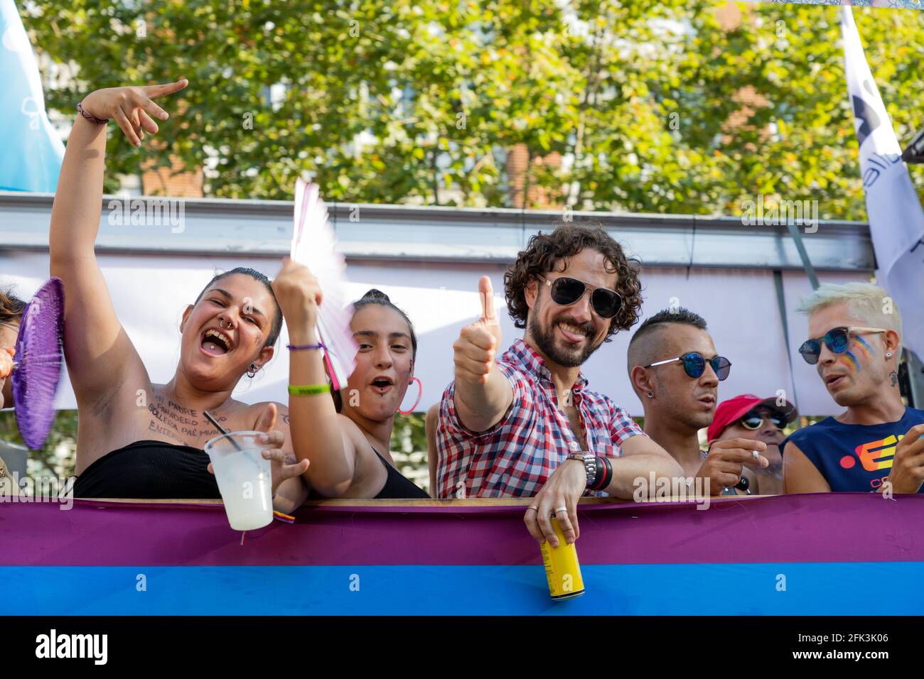 Barcelone – Espagne. 29 juin 2019 : Les participants à la parade applaudissent, agitent des éventails et font un signe de pouce levé depuis un char drapé de drapeaux lors de la Barcelona Pride. Banque D'Images
