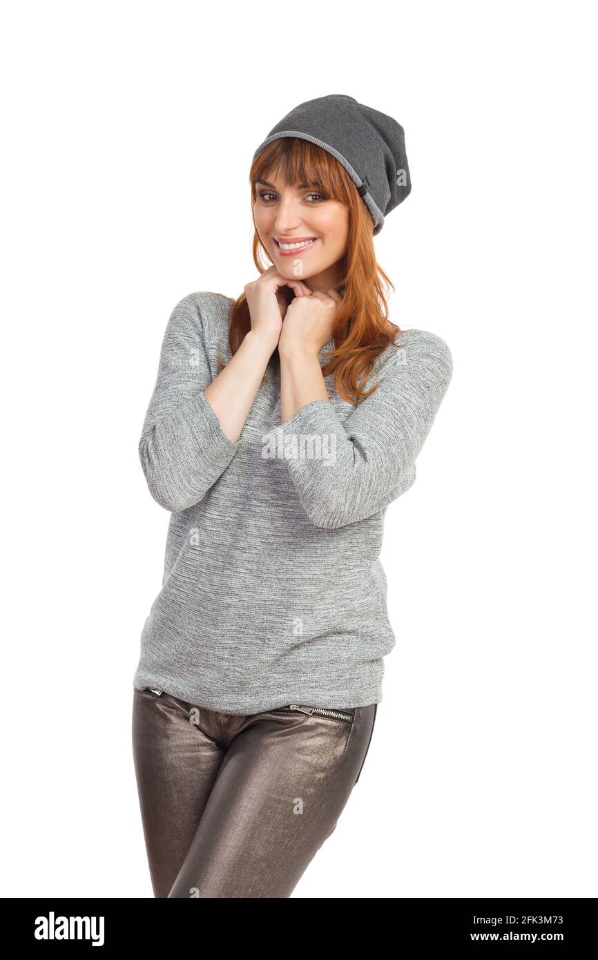 Portrait d'une femme mignonne en blouse grise, pantalon brillant et casquette d'hiver. Vue avant. Trois quarts de longueur en studio prises isolées sur blanc. Banque D'Images