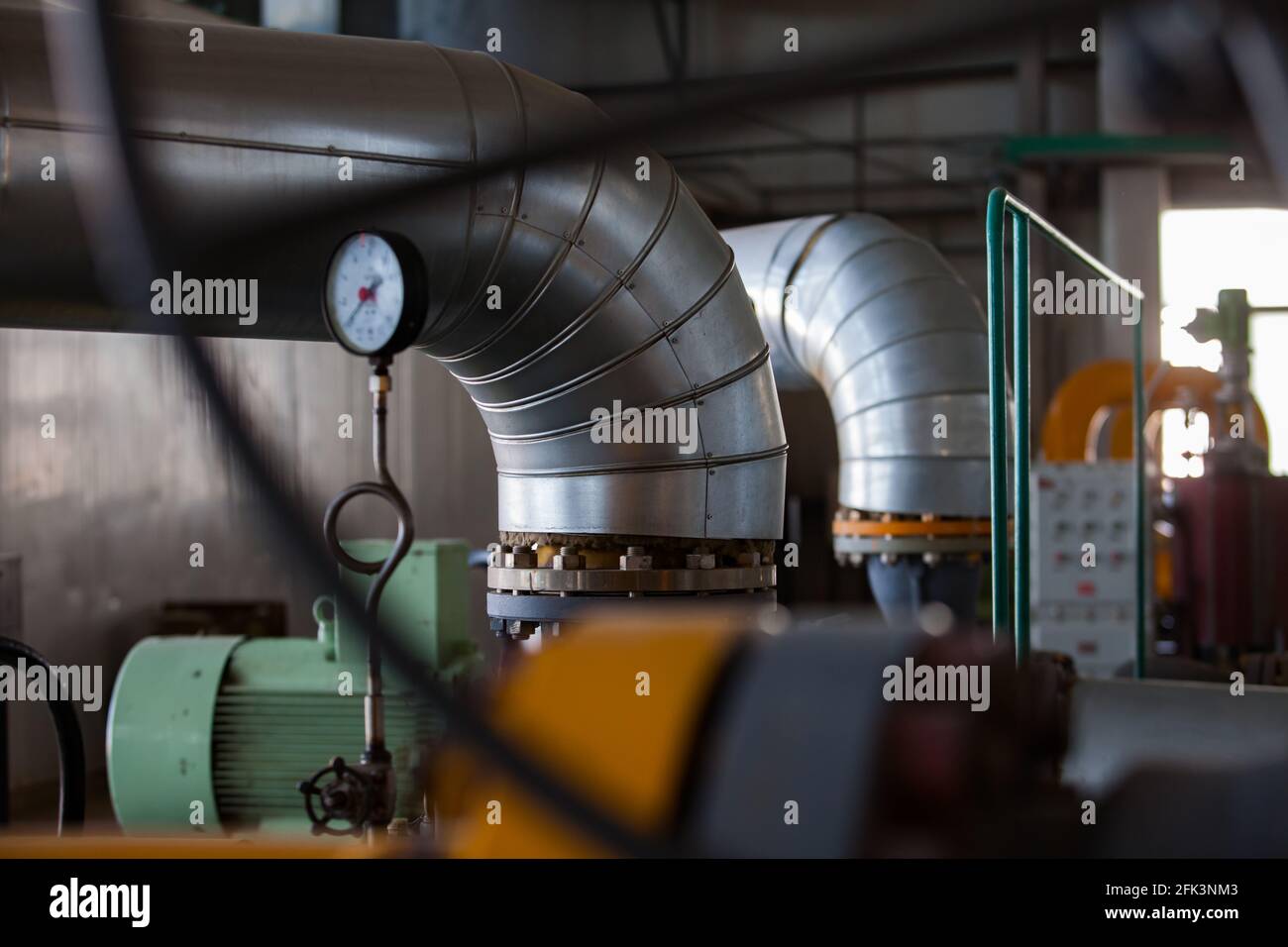 Isolation thermique en métal gris sur le tuyau (mise au point). Chaufferie. Manomètre et moteur électrique vert au premier plan, flou. Faible profondeur de champ. Banque D'Images
