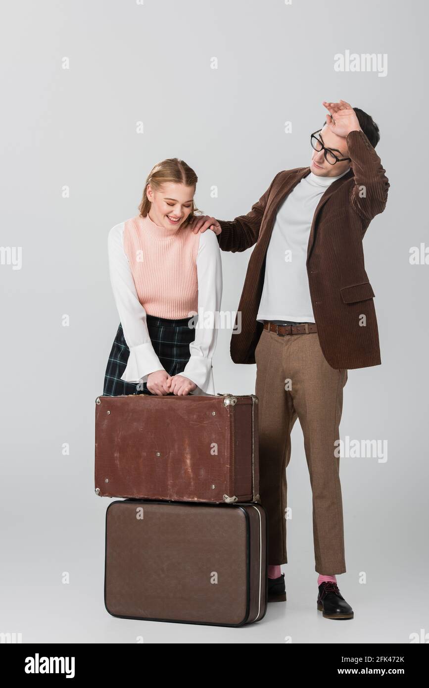 une jeune femme riant près de valises et un petit ami fatigué sur le gris arrière-plan Banque D'Images