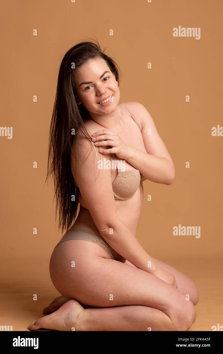 corps positif. Une fille en sous-vêtements beige pose sur un fond rose. Banque D'Images