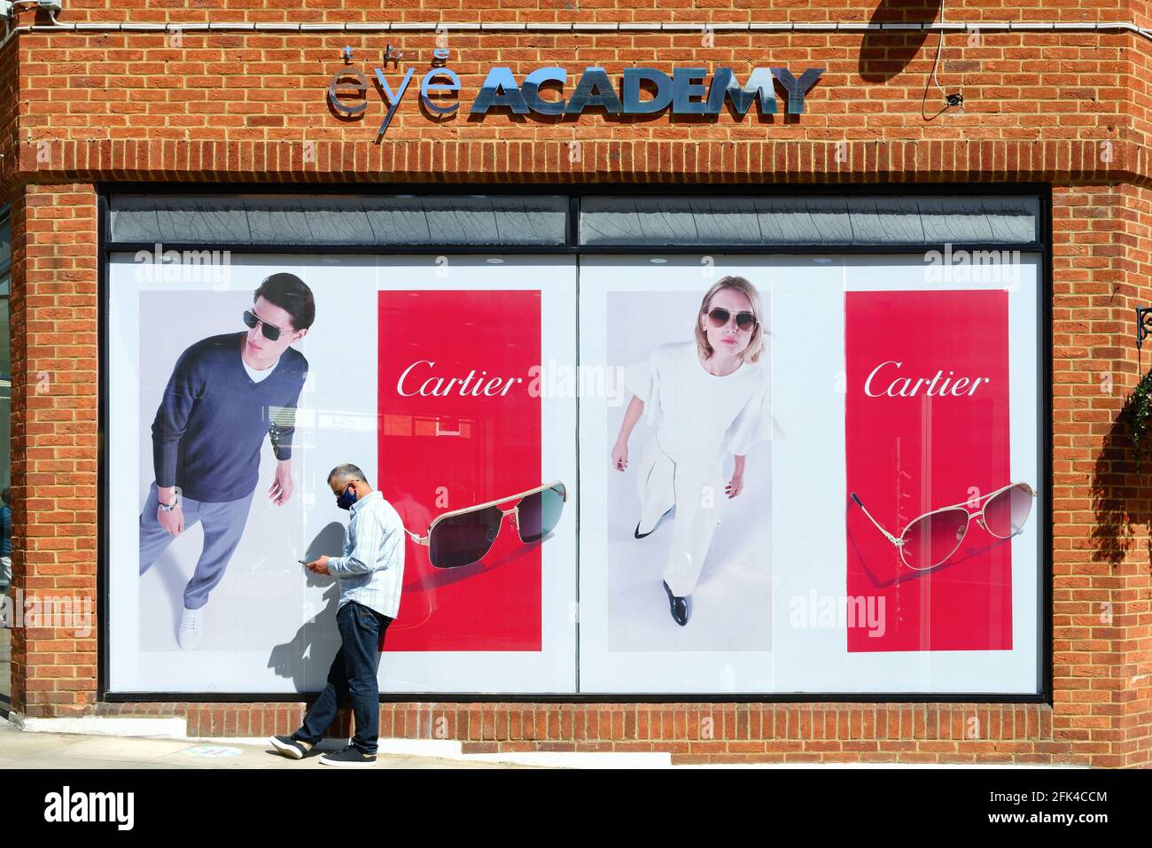 Un homme d'âge moyen utilisant un téléphone portable debout à l'extérieur Les opticiens 'Eye Academy' avec Cartier lunettes de soleil exposition derrière lui Banque D'Images