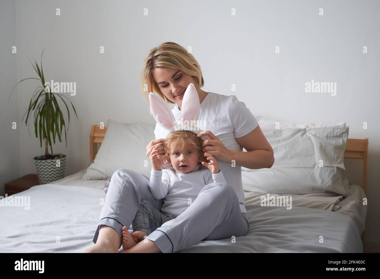 jeune maman et petit fils dans les oreilles de lapin ont le plaisir à la maison sur le lit Banque D'Images