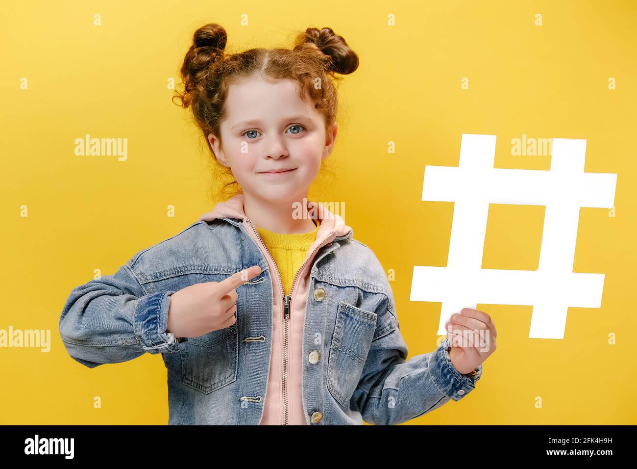 Portrait d'adorable et adorable petite fille adorable dans une veste en  denim pointant vers le grand symbole de hashtag blanc et souriant à  l'appareil photo Photo Stock - Alamy
