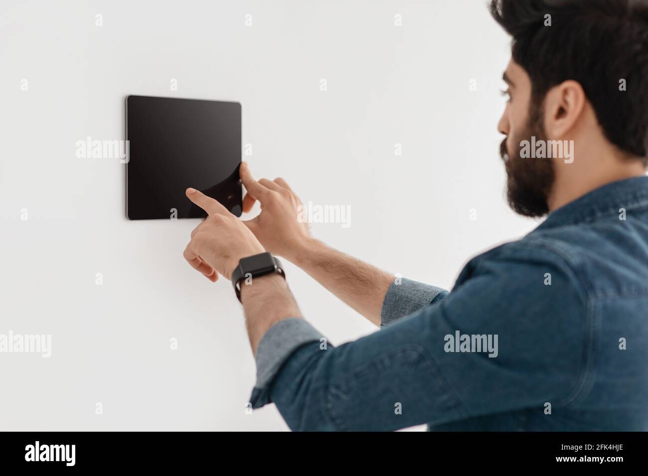 Technologie innovante pour l'appartement. Guy utilisant une tablette numérique au mur avec l'application Smart Home Control System Banque D'Images