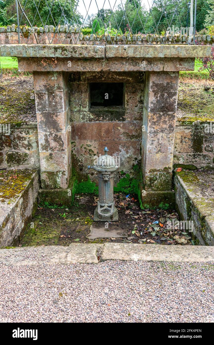 Une vieille fontaine d’eau potable en fonte, cylindrique avec nervures longitudinales, un dôme sur le dessus et un bec de lion sous un abri en pierre Banque D'Images