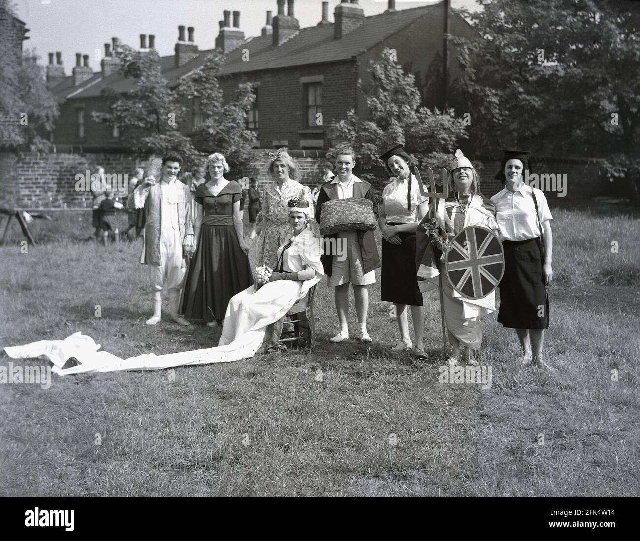 Dans les années 1950, historique, sur un terrain au bout de la terrasse des maisons victoriennes, un groupe d'hommes locaux - « The Heavy Gang » vêtu de vêtements pour femmes et de vêtements fantaisie debout pour une photo avant un spectacle pour le festival « Day », Angleterre, Royaume-Uni. Les acteurs amateurs ici sont en costumes différents, y compris Guinevere, la légendaire reine du roi Arthur. May Day était une tradition ancienne qui célébrait l'arrivée du printemps et de l'été et les artistes s'habillent et redonnent de vieux folklore et des histoires en dansant autour d'un grand poteau en bois, un maypole, une activité populaire. Banque D'Images