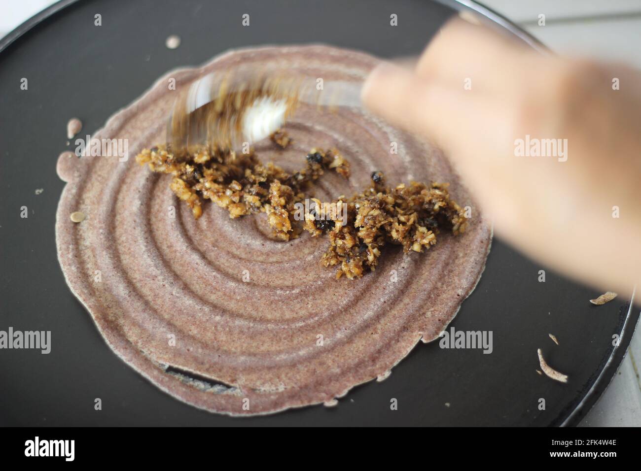 Étaler la pâte de millet sur une plaque chauffante. Des crêpes de millet de doigt dans la fabrication. Banque D'Images