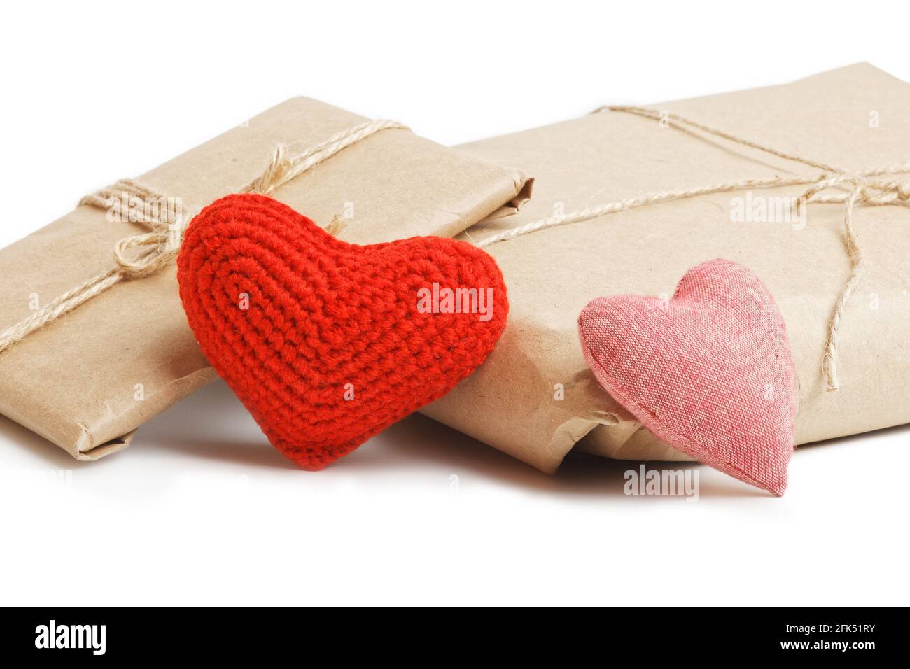 Deux colis de papier kraft attaché avec de la ficelle et de petits coeurs rouges faits à la main isolés sur fond blanc. Un cadeau pour la Saint-Valentin. Banque D'Images