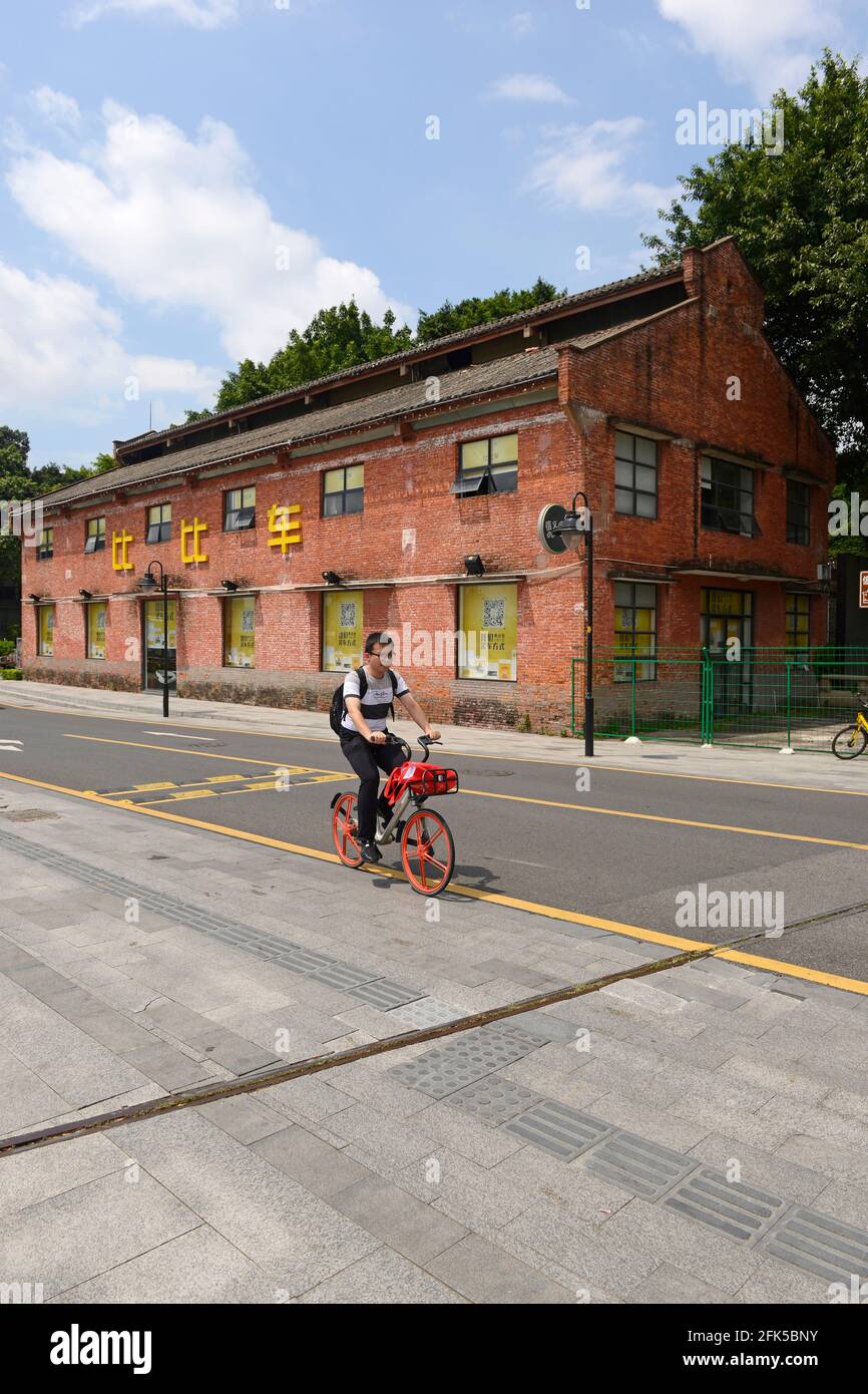 Un homme passe à côté d'un entrepôt préservé au bord de la rivière à Guangzhou, en Chine, sur un vélo de location. Banque D'Images