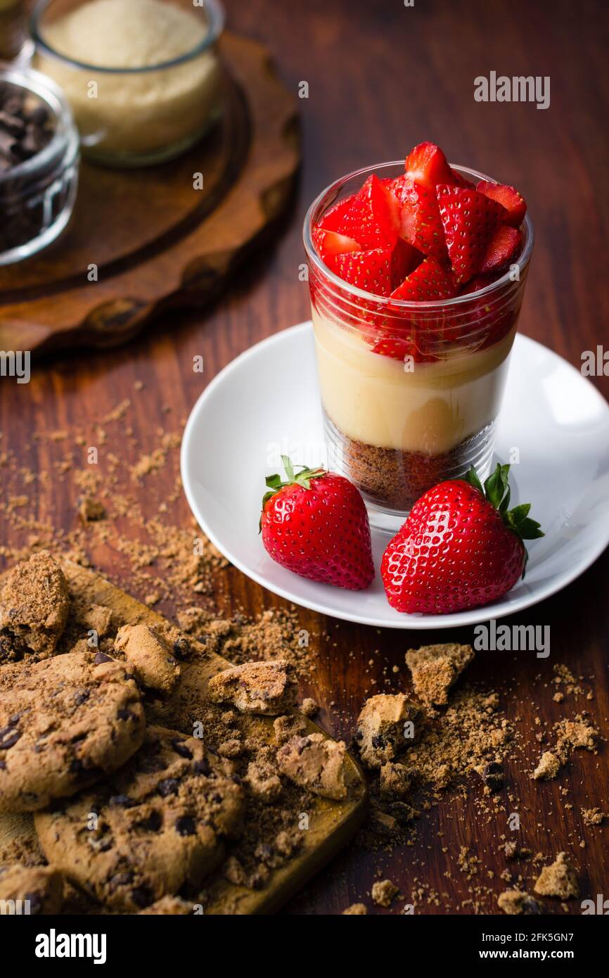 Dessert aux fraises avec pudding et biscuits sur bois sombre arrière-plan avec pots en verre Banque D'Images