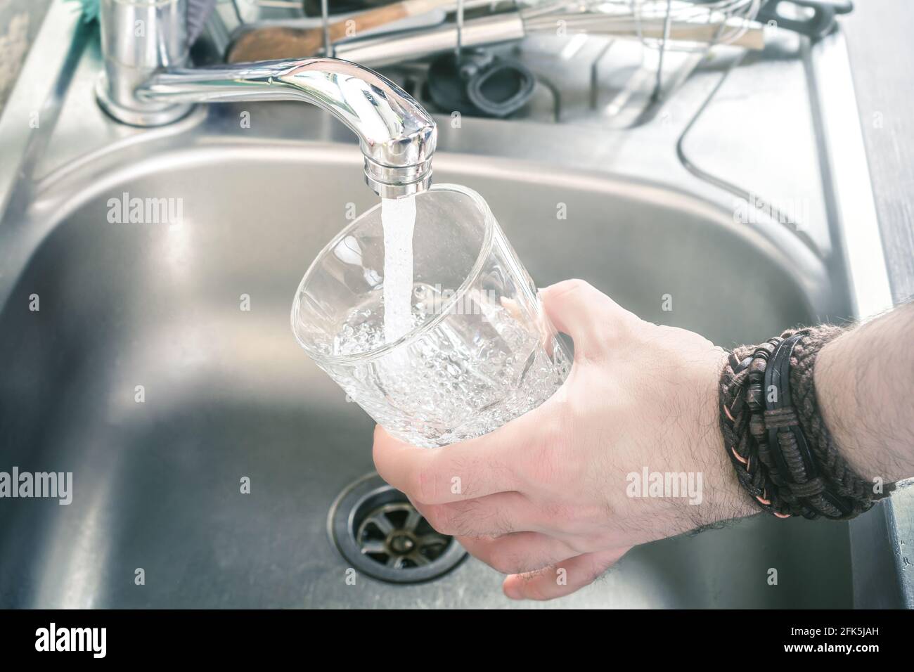 Homme tenant UN verre au-dessus de l'évier de cuisine le remplir Avec l'eau qui coule du robinet Banque D'Images