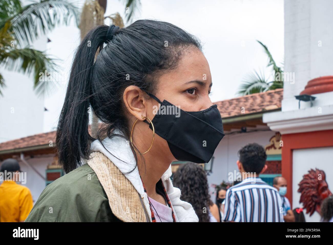 Guatapé, Antioquia, Colombie - avril 4 2021 : une jeune femme latina portant un masque noir est debout devant l'Église Banque D'Images