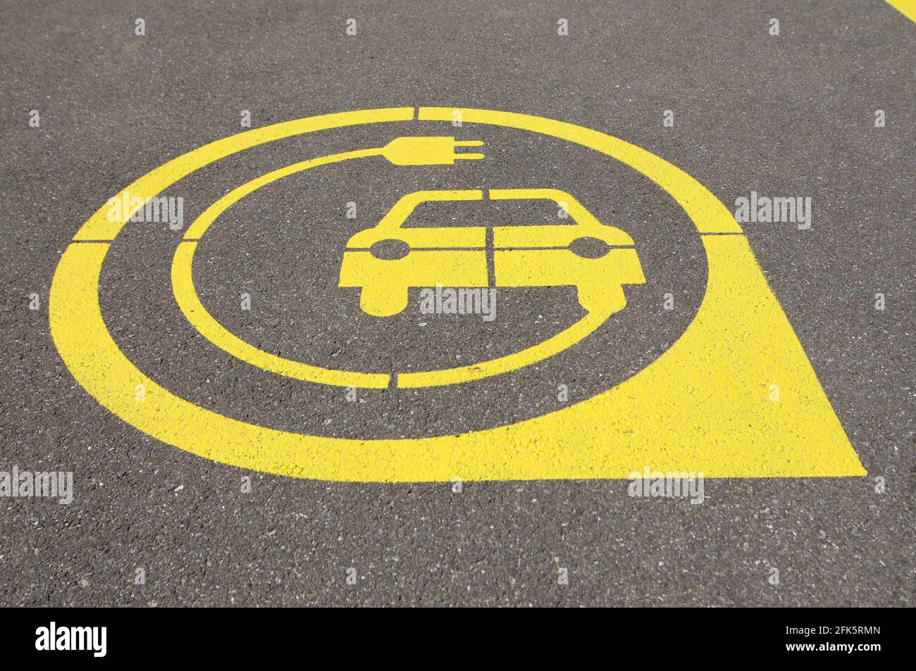 Vue à angle bas sur le symbole jaune de station de charge de véhicule électrique sur asphalte noir situé dans la ville de Zug, Suisse Banque D'Images