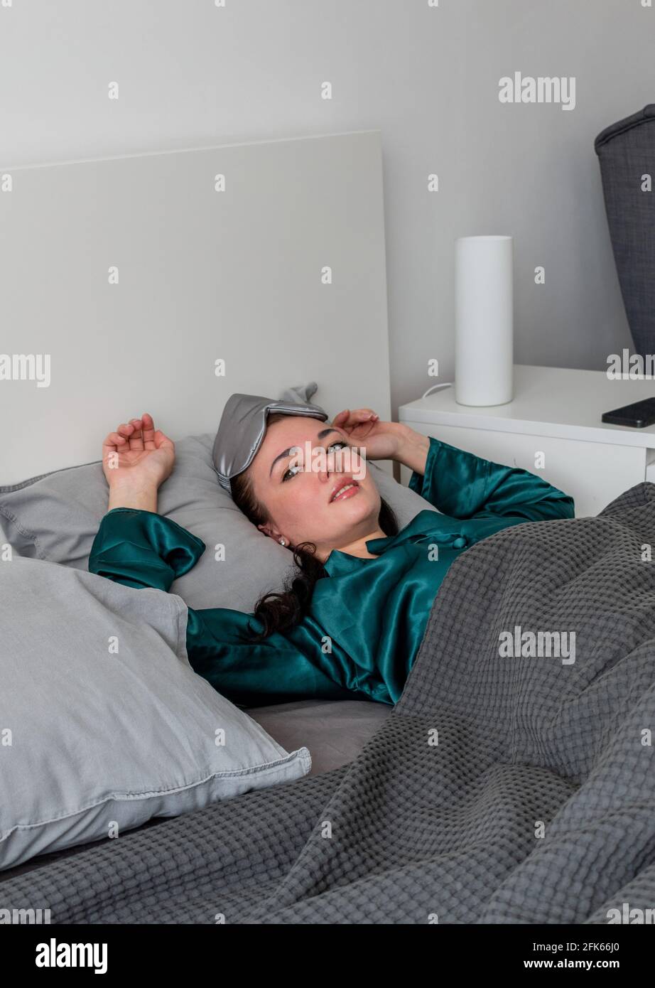 Une jeune femme en pyjama de soie repose dans un lit confortable et doux. Bien-être à la maison. Concept bien-être. Banque D'Images
